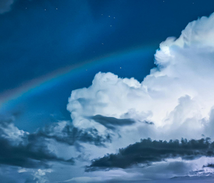 Clouds and Rainbow on Sky with Lightning behind.